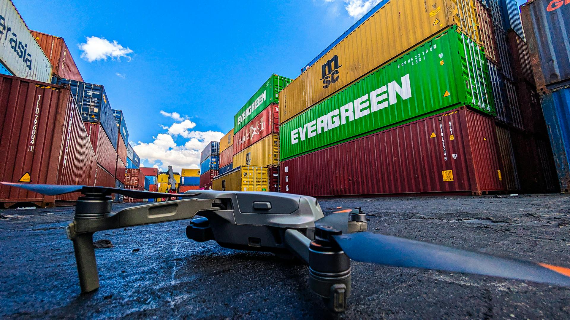 Drone on ground near colorful stacked shipping containers under bright blue sky.