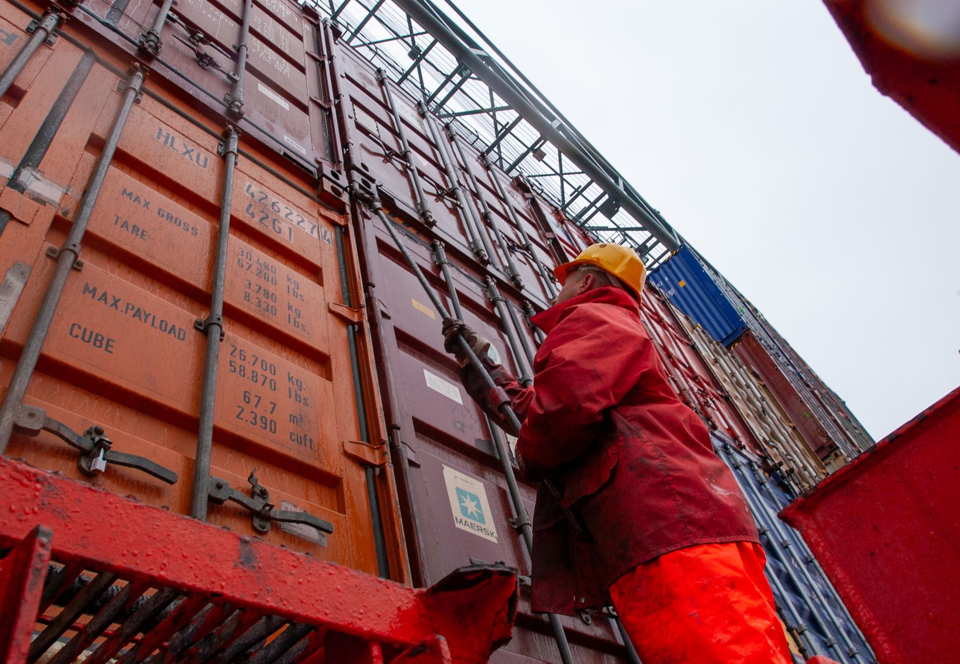 Industrial worker securing cargo containers on a rainy day at a shipping port.