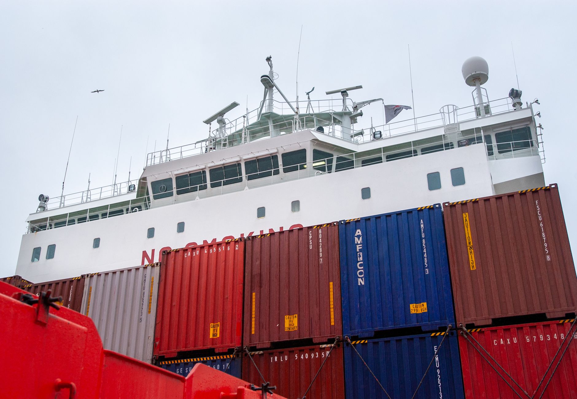 Close-up of a container ship with colorful shipping containers against a cloudy sky.